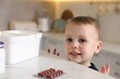 © New Africa - Child safety at home. Little boy playing with pills at table in kitchen, closeup