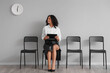 © Pixel-Shot - Female African-American job applicant waiting for interview near light wall