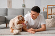 © Pixel-Shot - Young man with cute Australian Shepherd dog lying on carpet in living room
