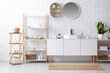 © Pixel-Shot - Chest of drawers, sink and shelving unit with towels and sprays near white brick wall in bathroom