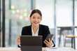 © David - Asian businesswoman holding phone work on laptop computer  at the office with calculator document doing planning analyzing the financial report, business plan investment, finance analysis concept.