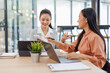 © David - Smiling two asian accountant women working with documents using calculator and laptop computer at office desk