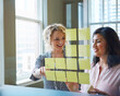 © peopleimages.com - Glass wall, women and smile with sticky notes in meeting for story ideas, planning and workflow. Team, journalists and discussion in newsroom for article planner, news development or task management