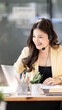 © NAMPIX - Close-up of a smiling Asian female customer service agent wearing a headset and working on a laptop in a modern office.