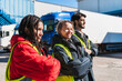 © Koldo_Studio - Diverse team of smiling truck drivers standing with arms crossed at a loading dock, ready for work in a cold storage facility
