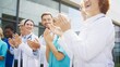 © VAKSMANV - Smiling medical staff clapping hands while standing outside clinic under bright daylight. Confident group celebrating progress and sharing uplifting energy. Professionals enjoying supportive moment.