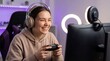 © Bilal - Portrait of a young female gamer sitting at a computer desk, wearing headphones and smiling at a webcam