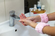 © Iryna - Close-up of woman's hands being washed. Female hands being washed under running water in the bathroom, promoting hygiene and cleanliness, with pink wristbands and soap visible.