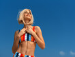 © SHOTPRIME STUDIO - fit young woman wearing colorful striped bikini top standing outdoors under clear blue sky, looking up with confident smile, summer lifestyle concept