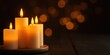 © T A Rima - Three lit white candles on a wooden plate with a dark background and warm glowing bokeh lights around them creating a cozy ambiance