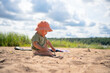 © Sk Elena - A toddler plays on a sandy beach wearing an orange hat, enjoying the warmth and freedom of outdoor play.