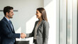© AK - A smiling businessman and businesswoman shaking hands in a modern office setting.