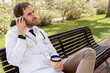 © StockMe - Doctor or healthcare worker finding a moment of rest outdoors during a demanding shift, communicating on a smartphone and holding a takeaway coffee cup