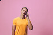 © SHOTPRIME STUDIO - Man wearing casual yellow t-shirt talking on mobile phone, looking at camera, indoor studio shot with simple pink background, lifestyle concept, communication, leisure, modern fashion