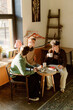 © m-art - Three friends sit around a small table in a warm cafe, sharing laughter and coffee. Sunlight streams through the window, creating a comforting atmosphere perfect for conversation.