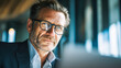 © Daria - Portrait of confident mature businessman with glasses in formal suit working thoughtfully inside modern office space by large windows during daytime