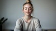 © Yuliia - Young blonde woman with closed eyes in cozy gray sweater practicing mindfulness meditation at home. Peaceful relaxation and mental wellness concept.