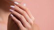 © onlyAW - A woman's manicured hand with white nails rests on her knee against a pink background.