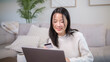 © wattana - Smiling woman using a credit card for online shopping on her laptop at home.