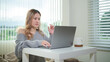 © wattana - Young woman enjoying online work or study on a laptop in a bright living room. Freelance, remote job, and home office lifestyle concept.