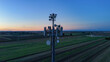© august.columbo - Cell tower transmitting modern telecommunication signals and 5G network connectivity over fields during a calm blue hour sunset