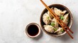 © Honey - A bowl of dumplings with chopsticks and a side of soy sauce on a white surface
