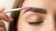 © NENI - Close-up of a hand using a pink spoolie brush to shape and style a perfectly groomed eyebrow