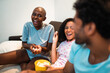 © Nexa - Diverse group of happy friends laughing and eating popcorn during a movie night at home.