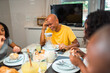 © Nexa - Happy African-American man laughing while having breakfast with his family at home.
