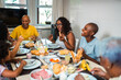 © Nexa - Happy multi-generational Black family enjoying a healthy breakfast together at home, laughing and talking around a table filled with fresh food.