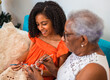 © Nexa - Happy African American grandmother teaching her young granddaughter how to crochet while sitting on a sofa at home, sharing a special intergenerational bonding moment.