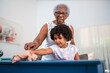 © Nexa - Senior African American grandmother and young granddaughter cleaning a blue table together at home.