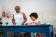 © Nexa - Happy African American grandmother and granddaughter spending time together at home during Christmas season, interacting at a blue table in a bright living room.