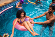 © Nexa - A joyful young woman laughing while floating in a pink ring as a man pushes her in a bright blue swimming pool during a summer day.