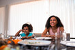 © Nexa - Happy African American young woman and child sitting at a dining table during a family meal at home.