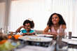 © Nexa - Happy African American sisters sitting at a dining table during a family meal at home.