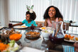 © Nexa - Happy African American sisters laughing and enjoying a healthy meal together at the dining table at home.