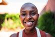 © Nexa - Close-up portrait of a happy young Black woman with a shaved head smiling outdoors.