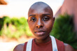 © Nexa - Close-up portrait of a beautiful young Black woman with a shaved head looking directly at the camera outdoors.