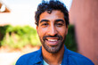 © Nexa - Close-up portrait of a happy young man with dark curly hair and a beard smiling at the camera outdoors.