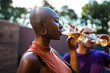© Nexa - Young Black woman with shaved head drinking cold beer at an outdoor social gathering during sunset.