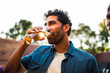 © Nexa - Relaxed Middle Eastern man enjoying a refreshing glass of beer at an outdoor social gathering during golden hour.