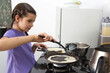© Evgeniia Primavera - Girl carefully pouring pancake batter onto hot frying pan while cooking homemade breakfast on kitchen stove during focused learning and family food preparation process