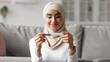 © Prostock-studio - Female health, ovulation, expecting baby and good news. Close up portrait of happy glad pretty millennial arab woman in hijab looking at positive pregnancy test in living room interior, free space
