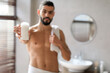 © Prostock-studio - Handsome young guy stands shirtless in a stylish bathroom, holding a tube of deodorant close to the camera. He presents the cosmetic product with a confident smile against a blurred background.