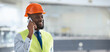 © Prostock-studio - A man wearing a safety vest and hard hat is speaking on his phone while standing in a construction site. He appears focused and engaged in conversation while overseeing work.
