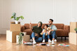 © Prostock-studio - Portrait of smiling muslim family sitting on the floor leaning on couch in new apartment, doing repair. Cheerful woman in hijab pointing finger aside, people choosing wall color and interior design