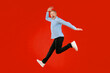© Prostock-studio - A man with gray hair and a blue checkered shirt jumps in the air with an excited expression. His black pants and white shoes contrast with the bright red background. The scene shows joy and energy.