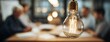 © Snowstudio - Light bulb hanging in modern office above people in meeting, symbolizing creative thinking