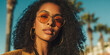 © Selvi - Black woman with curly hair wearing stylish sunglasses and gold hoop earrings in a sunny outdoor setting